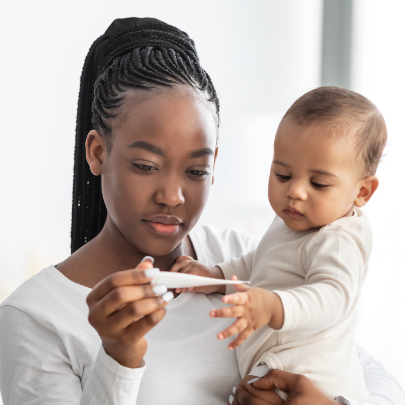 Mother with baby holding a thermometer as the child has a fever